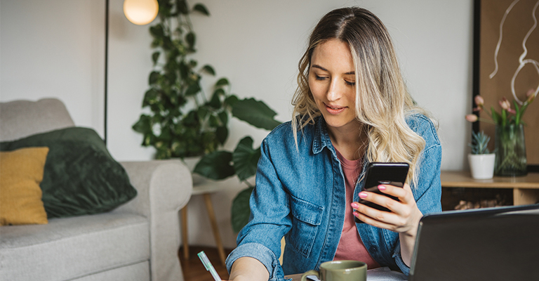 woman referencing phone while taking notes
