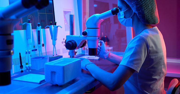 a woman in lab setting looking through a microscope