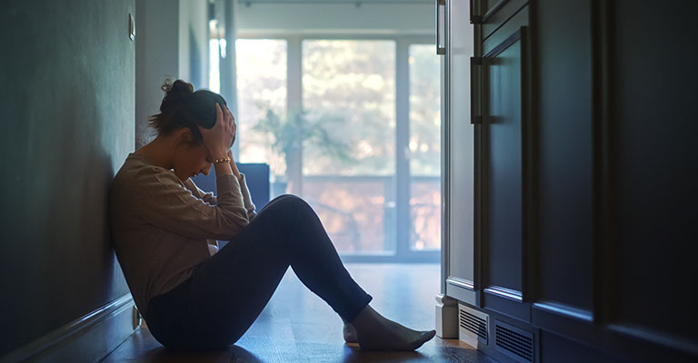 a stressed woman with her head in hands, seated in the hallway