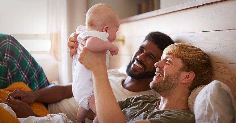two fathers smiling and lifting up their baby