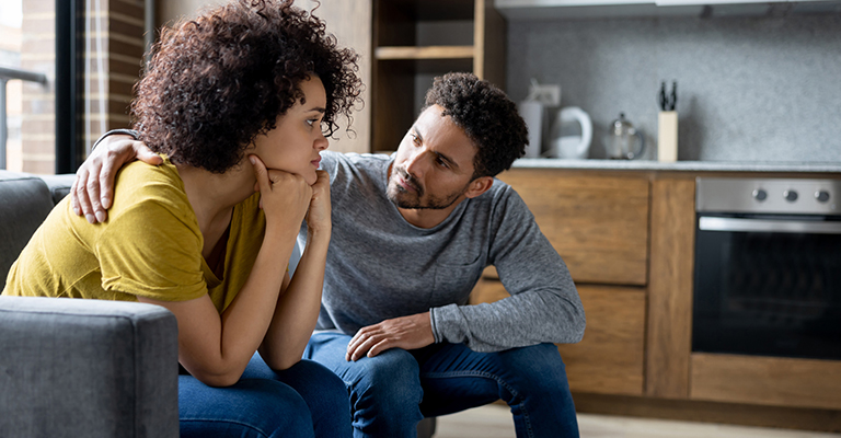 pair seated on couch, with one partner comforting his stressed female partner