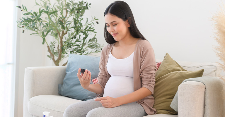 pregnant woman checking blood sugar seated on couch