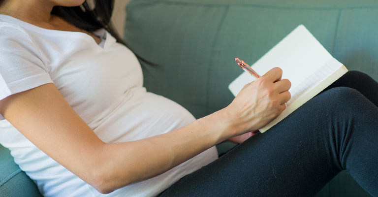 seated pregnant woman writing on the couch