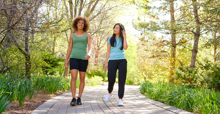 two friends walking on paved trail in forest