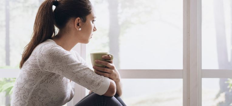 woman with coffee peering out the window
