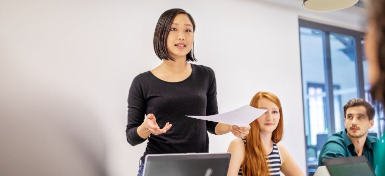 standing woman presenting at table with seated colleagues