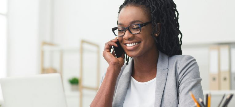happy Black woman on phone while looking at laptop